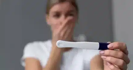 Femme blonde tenant un test de grossesse avec une expression surprise