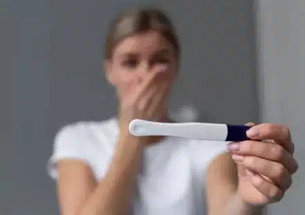 Femme blonde tenant un test de grossesse avec une expression surprise